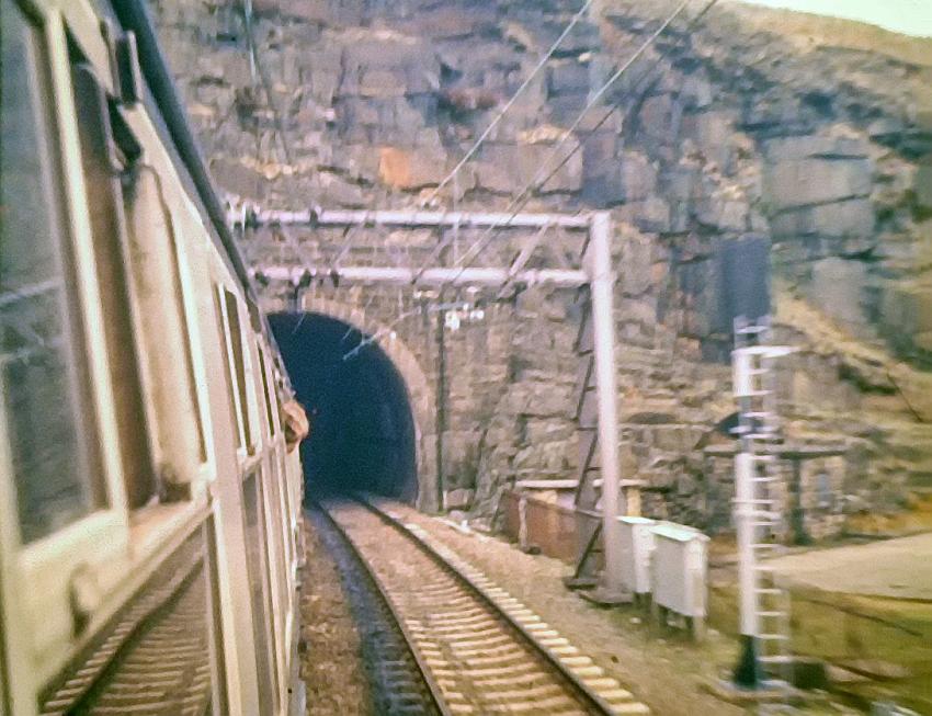 Entering the Woodhead tunnel from the west - this is the one and only main Trans Pennine railway to have been lost. The view shows a look along the carriage as the train enters the tunnel. The overhead cantenary system is quite visible and a signal can be seen on the line heading in the Manchester direction.