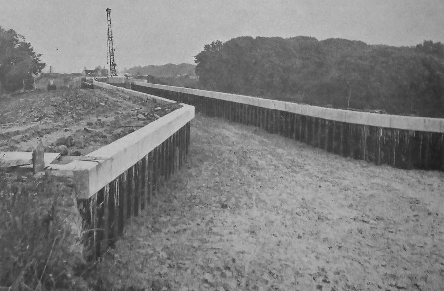 View of the rebuilt canal structure over the Bolin valley. On either side of the canal bed is piling, topped by concrete. A crane can be seen on the canal bed further along.