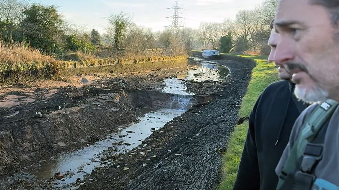 Chris Tate and his friend view the stricken canal section. A huge chasm where the canal once stood can be seen. The grey widebeam boat can be seen in the distance.