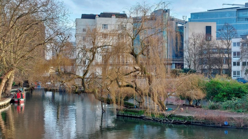 Little Venice - London's popular tourist destination with the large pool and boats in it evident. In the background visible through the trees can be seen the Battleship building. This is winter and its the part of the year when both the Battleship building and the Little Venice pool can be seen easily from each other.