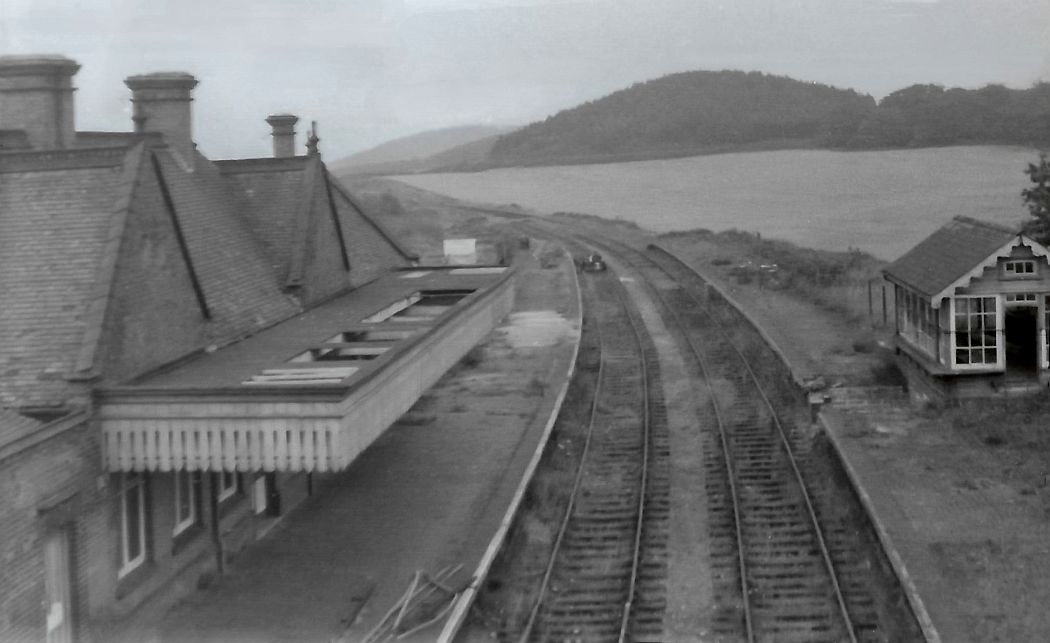 A Weybourne before and after from the author. This picture is taken c1972. The railway station is in a generally derelict condition. The tracks curve away towards the left into the distance. There is a hill in the background and it is basically unchanged even today. The North Sea can just be seen in the distance.