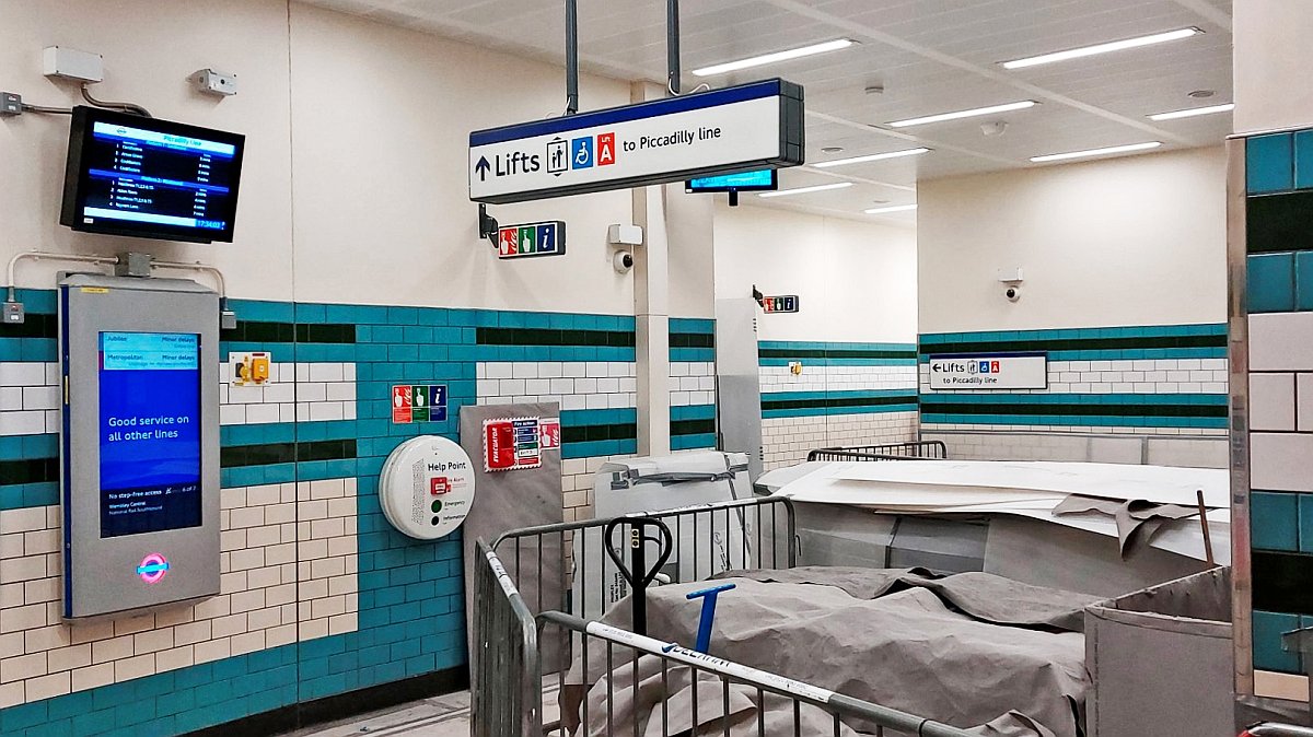 View of the Hooper's Court entrance lobby and lift areas. This was at a time when a fair bit of work was still underway down below in the deep level parts of the station and this street level area was in use for storage. Electronic indicators for Piccadilly line services can be seen at left. Signage for the lifts to the tube can be seen suspended from the ceiling. The colour scheme is modern (blue, green and cream but follows the original used in 1907).