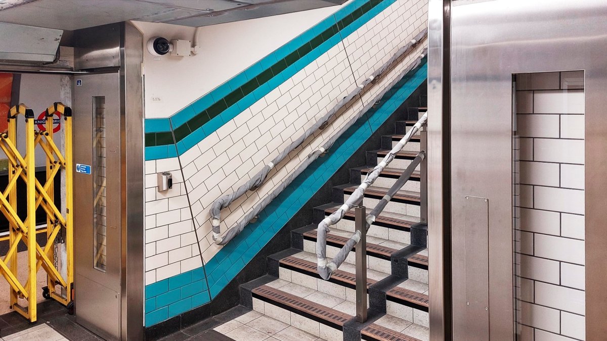 The new stairs up to intermediate level showing the brand new tiles - colours green, blue and cream - that will match the older ones that will remain in use in parts of the upgraded station. The stairs are not in use yet they are blocked off by yellow barriers seen at right.