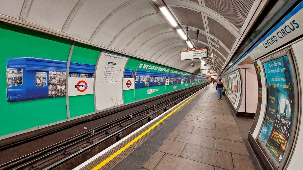 Oxford Circus northbound platform with its very long advert. Lots of green and blue on the left side and an almost empty station platform with the tube tracks stretching in to the distance.. A Victoire line route map and station roundels can be seen at left too.