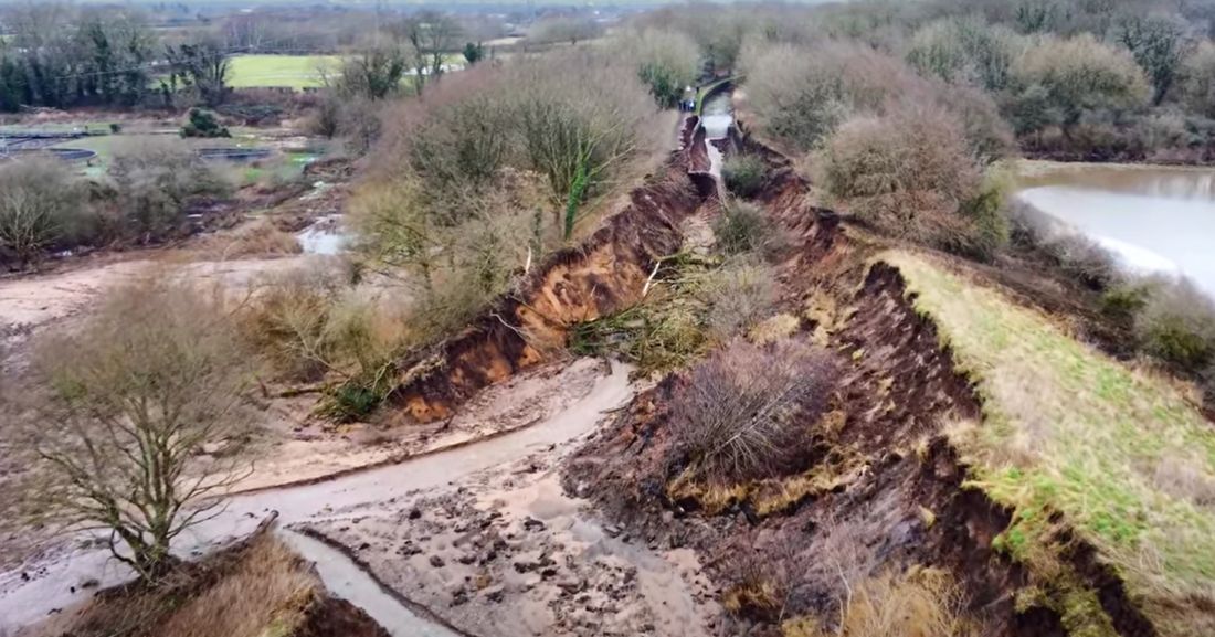 Scene of the breach showing the different colours and the sandy bits are quite evident in the centre of the picture. Many trees abound, some fallen into the breach.