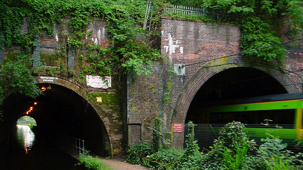 A close up view of the twin tunnels at Edgbaston. On the left is the canal tunnel and on the right is the electrified railway tunnel. A train has just emerged from the tunnel and its heading for Birmingham New Street station. The electric lights in the canal tunnel itself are prominent.